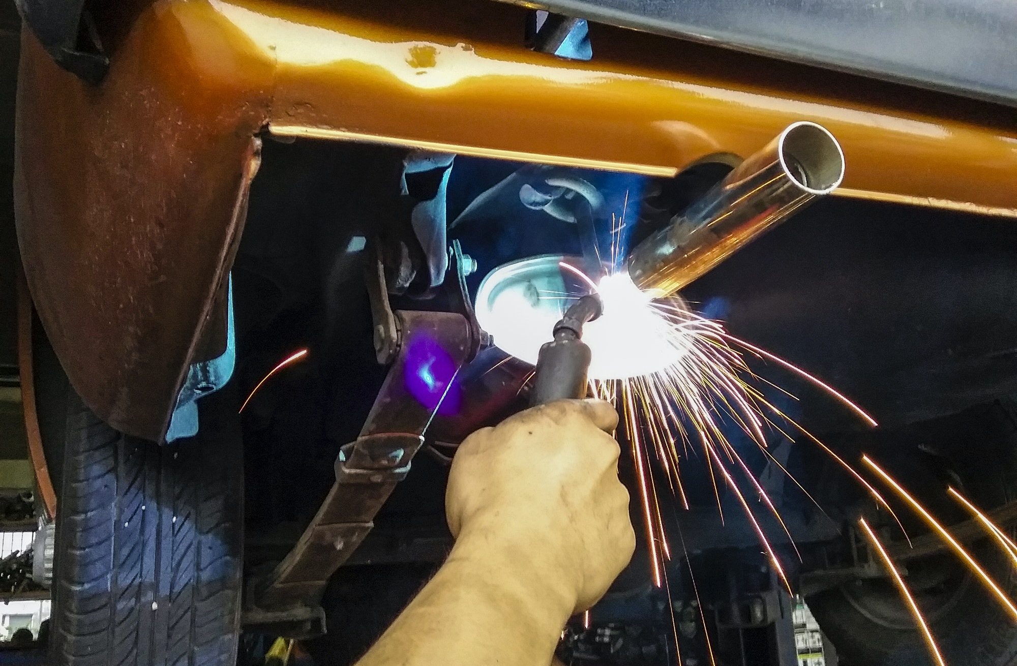 Closeup of blue collar worker welding classic car muffler